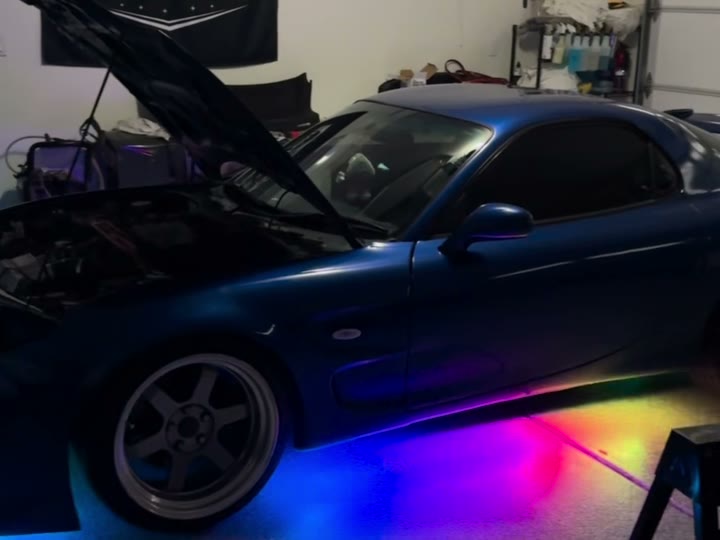 Blue RX-7 in the shop with rainbow underglow spilling out from under the sills across the floor